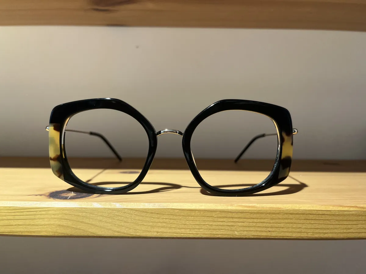 Montura de pasta negra y carey, de forma hexagonal, sobre una balda de madera clara